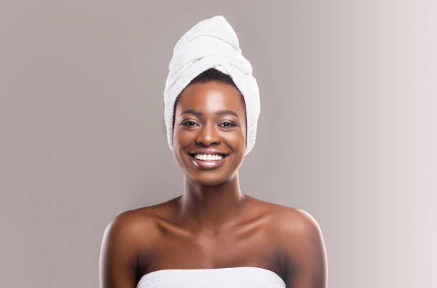 Beautiful young woman wrapped in white bath towel preparing for sauna, grey studio background