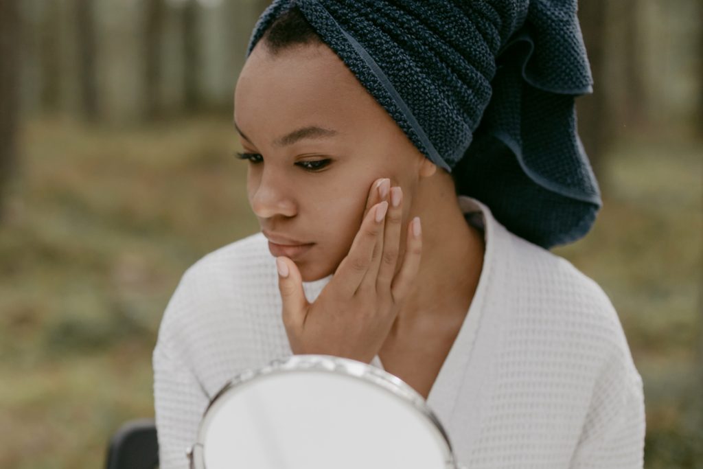 Woman holding the side of her face, while looking in mirror. Laser Hair Removal in New Jersey